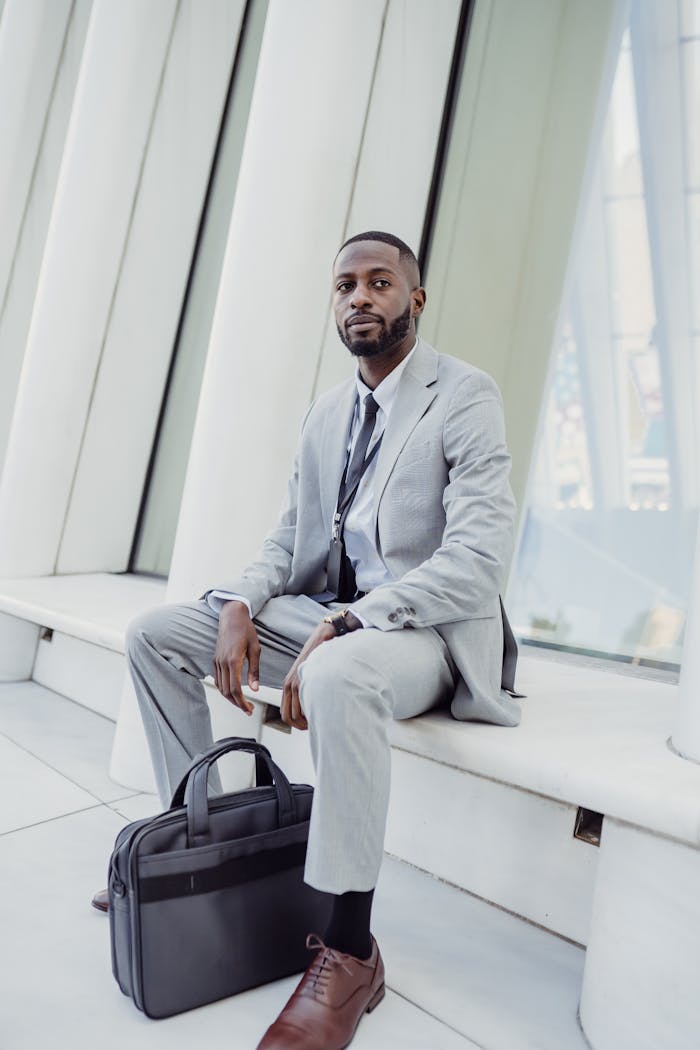 about-us-02 Businessman in suit sitting with laptop bag in modern architecture setting.