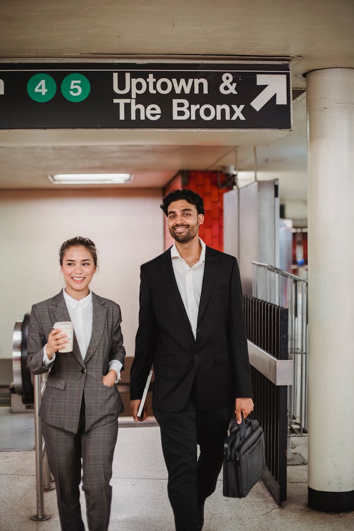Two smiling professionals walking in a New York subway station, holding coffee and briefcase.